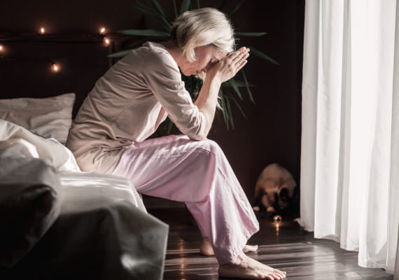 Woman sitting on the bed with her hands on her forehead.